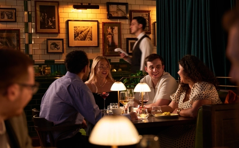 Group of customers dining together at a restaurant table while a server walks through the dining